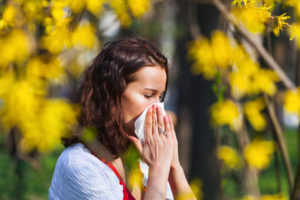 Woman surrounded by spring flowers blows her nose